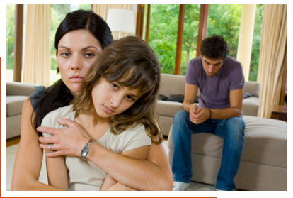 Woman holding child, with man looking on from background